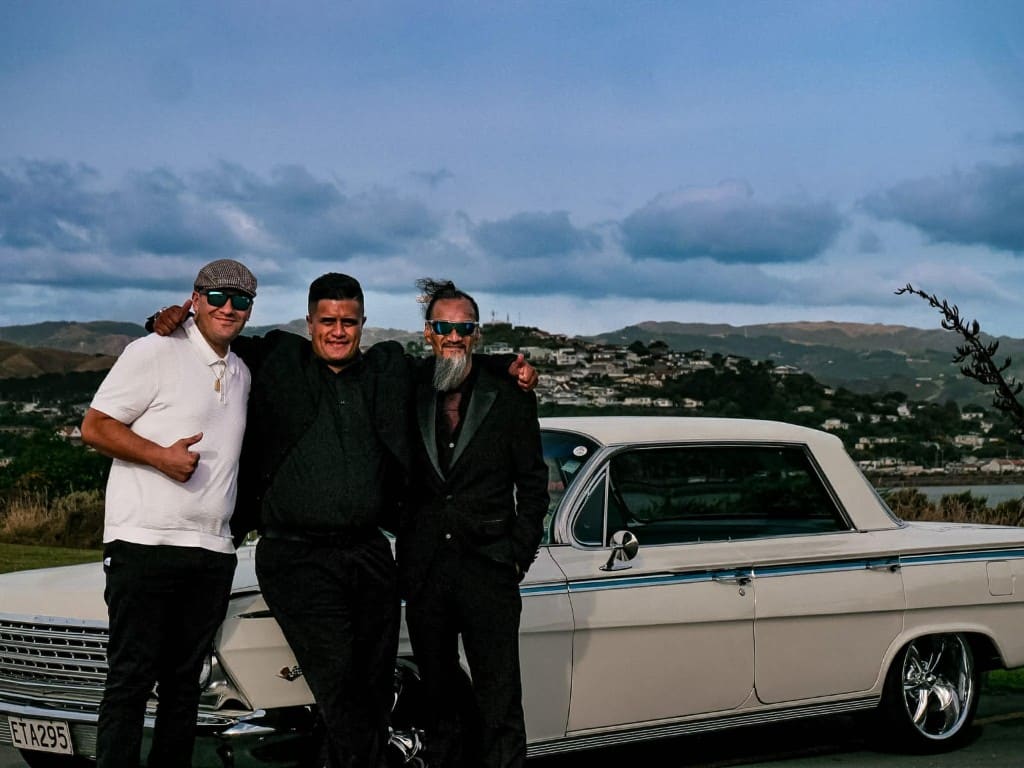 The white Impala parked above the harbour, with Liam and two others in front of it.